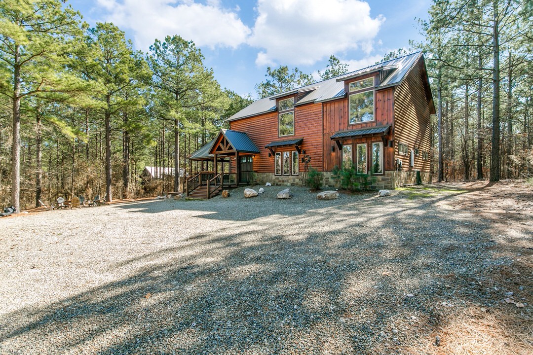 A cozy log home nestled in the woods, featuring a gravel driveway, ideal for lodging in Broken Bow, Oklahoma.