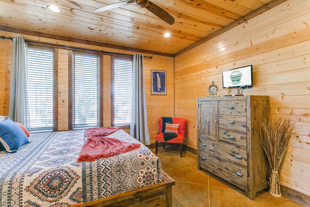Cozy bedroom in a Broken Bow cabin featuring a bed, dresser, and ceiling fan for a comfortable stay.