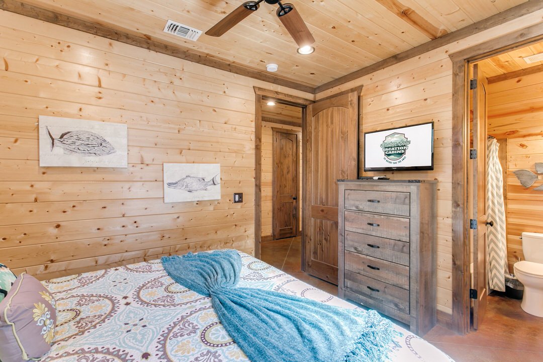 Charming cabin bedroom in Broken Bow, showcasing a bed, television, and ceiling fan for a restful experience.