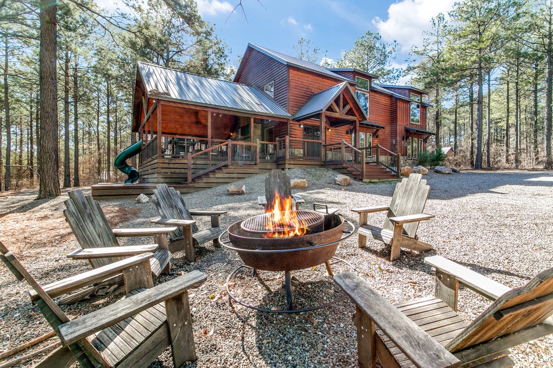 A cozy fire pit in front of a cabin in Broken Bow, Oklahoma, surrounded by chairs for a warm gathering.
