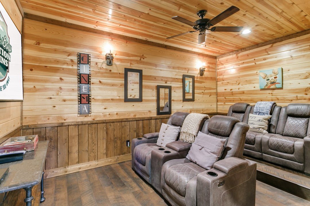 Interior of a Broken Bow cabin home theater, showcasing leather recliners and a ceiling fan for a relaxing experience.